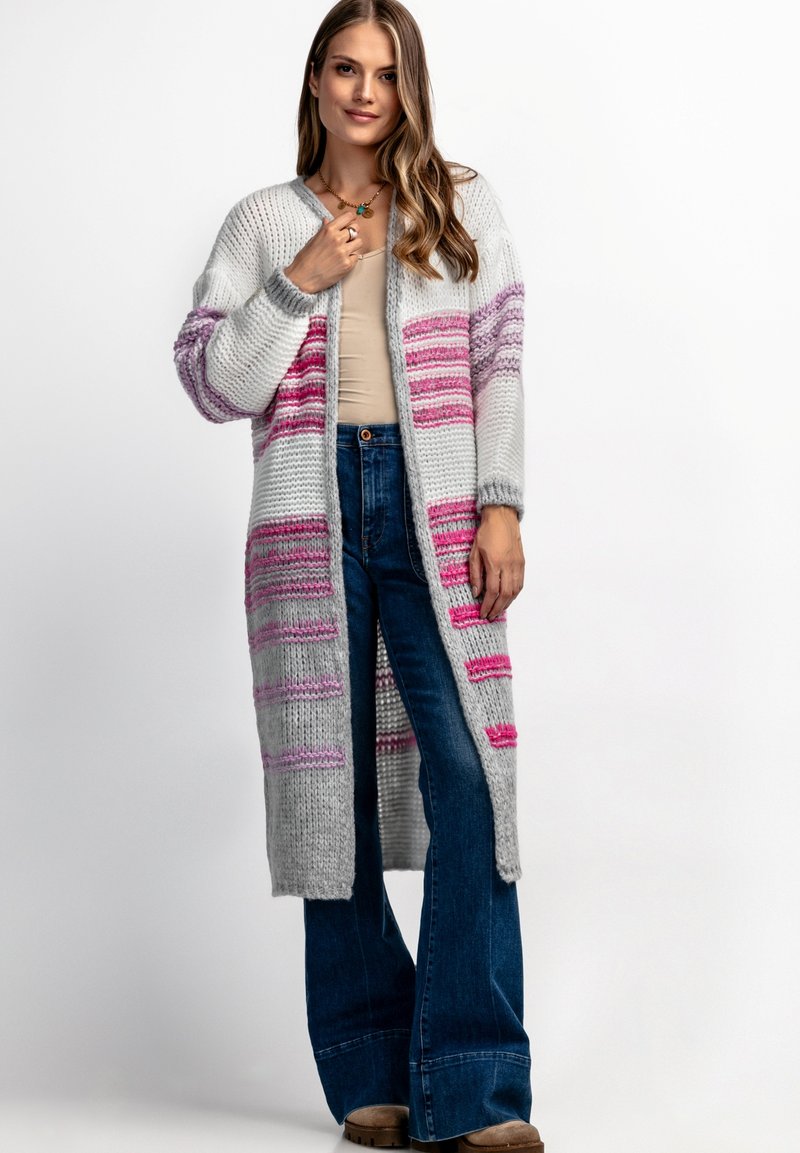 Długi sweter kardigan w kolorze szarym z różowymi i fioletowymi paskami; ma otwarty przód, ściągacze oraz teksturowany wzór. Nosi się go na beżowy top.