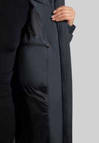 Giacca nera trapuntata con tasca interna con zip, texture morbida e interno liscio e foderato. Presenta un colletto strutturato e un design elegante.