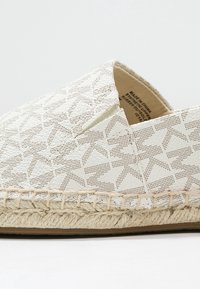 Espadrille blanca con una tela texturizada que presenta recortes geométricos. Detalles de cuerda de yute natural a lo largo de la suela. Diseño de punta cerrada.