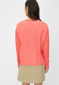 Korálová košile s dlouhým rukávem a kulatým výstřihem, volný střih a hladká textura, doplněná béžovou sukní s zadními kapsami a rovný střih.