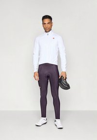 Roupa de ciclismo composta por uma camisola branca de manga comprida e leggings justas roxo escuro. Os acessórios incluem um capacete de ciclismo e sapatos brancos.