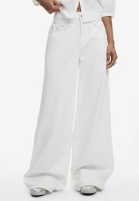 Jeans blancos de pierna ancha en tejido resistente, con bolsillos y cintura alta, con una textura suave y un diseño minimalista.