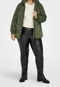 Doudoune vert olive avec capuche, pull blanc texturé, leggings en simili cuir noir avec fermetures éclair et bottes noires à lacets.