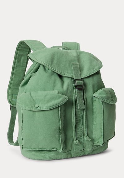Πράσινο σακίδιο καμβά με κλείσιμο με καπάκι, λουρί με αγκράφα, δύο μπροστινές θήκες με κουμπιά πίεσης και επενδεδυμένους ιμάντες ώμου.