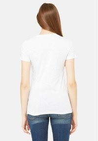 T-shirt en coton blanc à manches courtes, avec un col rond et une coupe ajustée, associé à un jean bleu, vu de dos.