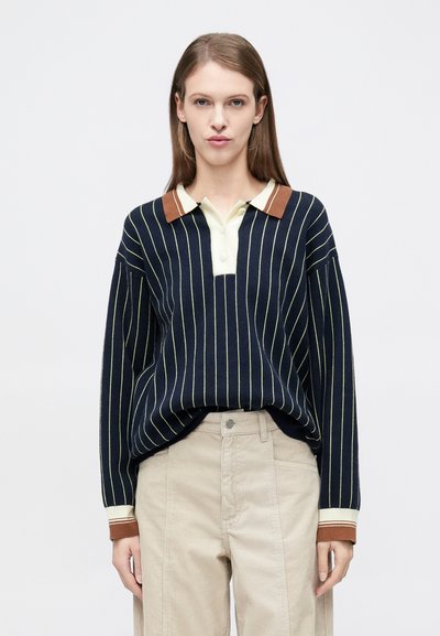 Pull-over marine à rayures verticales ivoire, col classique crème clair et marron ; larges manches, coupe décontractée, poignets côtelés. Pantalon en velours côtelé beige.