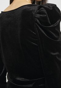 Black velvet dress featuring a scoop neck and puffed shoulder sleeves. The texture is smooth with a slight sheen, emphasizing its rich color.