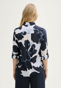 Zwart-witte blouse met abstract patroon en lichtblauwe accenten. Heeft een button-down kraag en opgerolde mouwen. Glad materiaal.