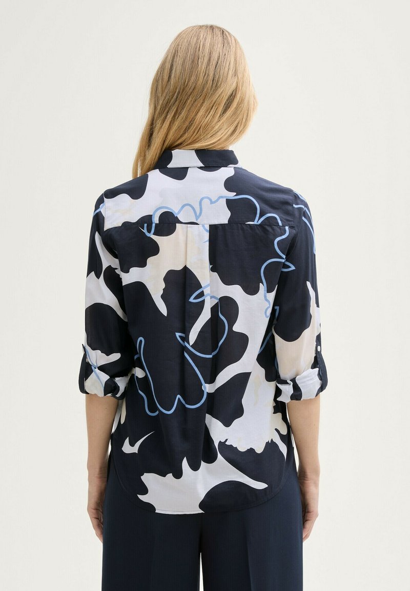 Schwarz-weiße Bluse mit abstraktem Muster und hellblauen Akzenten. Verfügt über einen Kragen mit Knopfleiste und hochgekrempelte Ärmel. Glattes Material.