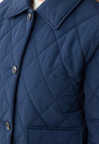 Giacca trapuntata blu navy con motivo a diamante, dotata di un ampio colletto e bottoni rotondi, realizzata in un tessuto morbido e leggero.