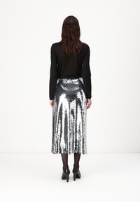 Zilveren pailletten midi rok met een aangesloten taille en een vloeiende vorm. Draag het met een zwart langemouwen shirt en gecombineerd met zwarte hakken.