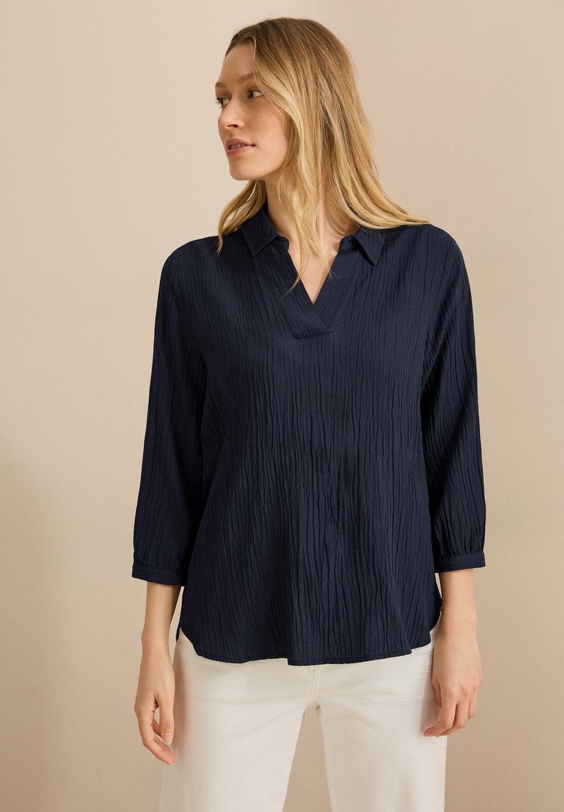 Marineblauw shirt met driekwartmouwen van een gestructureerde stof, met een kraag en een v-halslijn, en zijsplitten aan de zoom.