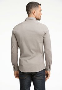 Maglietta grigia a maniche lunghe con colletto e polsini con bottone. Presenta una texture liscia e un design aderente. Indossata con jeans in denim scuro.