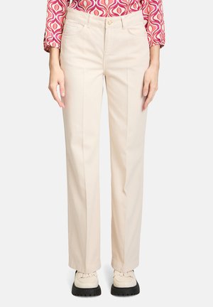 Beige Gerade-Hosen aus einem Baumwoll-Mix mit Fronttaschen und einem einzelnen Knopfverschluss, kombiniert mit hellen Schuhen.