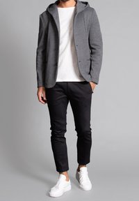 Blazer grigio con cappuccio realizzato in un tessuto testurizzato, abbinato a una t-shirt bianca e pantaloni neri slim-fit. Completato da sneaker bianche.