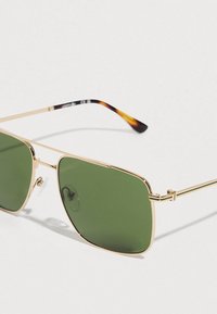 Gold metal-framed aviator sunglasses with green lenses and tortoiseshell-patterned temples on a white background.