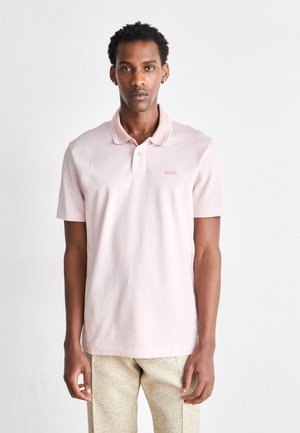 Lyserød polo-shirt med klassisk krave, to-knaps lukning og diskret hvid kant. Har et lille broderet logo på brystet.