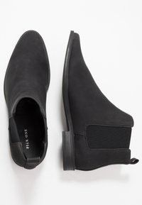 Botas negras hasta el tobillo de ante suave, con paneles laterales elásticos, puntera redonda y un tacón bajo y plano. Diseño sencillo, sin herrajes visibles.