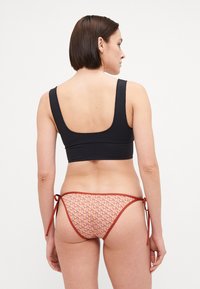 Top de bikini negru cu o bandă largă și bretele groase, asortat cu slipuri de bikini roșii cu un model, având șnururi pe laterale.