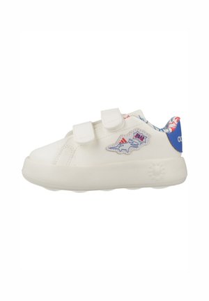 Zapatilla blanca para niños con dos tiras de velcro, pestaña azul en el talón y parche de dinosaurio en el lateral, con forro interior de colores.