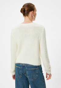 Maglione bianco morbido con scollatura rotonda e orlo a coste. Indossato con jeans blu a vita alta, che mostrano un look casual.