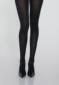 Collant opachi blu marina con una texture liscia, abbinati a décolleté neri con punta a punta, dotati di cinturini alla caviglia e dettagli in oro.