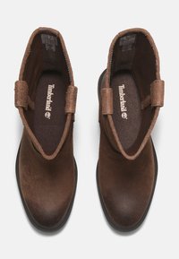 Botas de tobillo de ante marrón con un acabado suave, cuello texturizado y acentos laterales elásticos. Presenta una suela de goma negra y una plantilla acolchada.