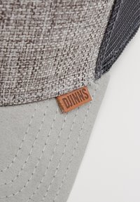 Gray and textured fabric cap with a light gray visor, featuring a brown leather tag embossed with "DJUNNS." Subtle stitching details are visible.