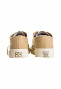 Sneakers in tela beige con profilo basso, punta rotonda, suola in gomma bianca, logo in rilievo sul tallone e upper in texture liscia.