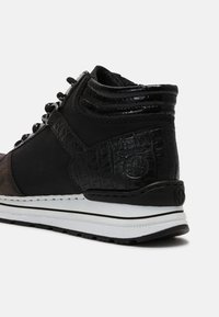 Baskets montantes noires avec talon en cuir texturé, col rembourré, semelle blanche à rayures noires et fermeture à lacets.