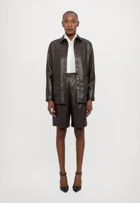 Mørk lærjakke med knappeåpning, skreddersydde shorts og en hvit skjorte. Glatt tekstur, minimalistisk design og ingen synlige mønstre.
