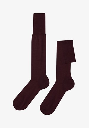 Par de calcetines altos hasta la rodilla de color marrón oscuro, uno completamente extendido y otro doblado en la parte superior, mostrados sobre un fondo blanco.