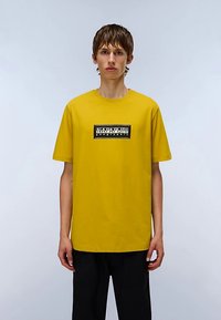 T-shirt gialla in cotone con scollo rotondo, maniche corte e logo rettangolare nero sul petto. Design semplice e vestibilità rilassata.