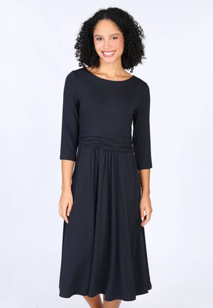 Schwarzes, langärmeliges Kleid aus weicher Stoffqualität, mit einer taillierten Taille und fließendem Rock, rundem Ausschnitt und subtilen Raffungselementen.