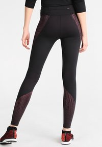 Leggings neri con un motivo geometrico testurizzato di colore rosso scuro sui lati. Presentano una vita alta e un design aderente.