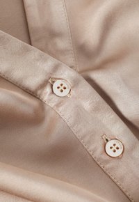 Beige satin tyg med en slät textur, prytt med två vita knappar. Varje knapp har fyra hål och texten "Titanium" tryckt på dem.