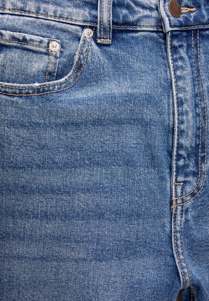 Jean en denim bleu avec une coupe droite, un design à cinq poches, des coutures orange contrastantes et des accents en métal.