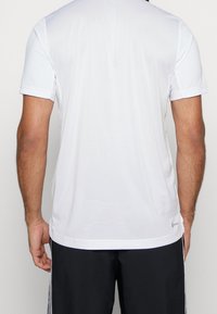 T-shirt blanc à manches courtes conçu pour le sport, avec un tissu en maille respirant, des coutures plates et un logo discret en bas de l'ourlet.