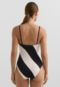 Černobílé pruhované plavky mají texturovaný povrch, úzká ramínka a střední vykrojení na stehnech a na zádech.