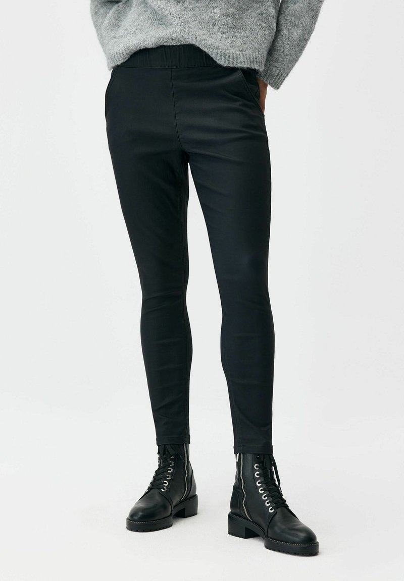 Czarne syntetyczne legginsy o gładkiej fakturze, dopasowanym kroju i elastycznym pasie. Dopasowane do czarnych botków sznurowanych przy kostce.