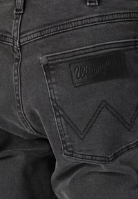 Achterzak van zwarte Wrangler-jeans met gestikt 'W'-ontwerp en leren merkpatch boven de zak.