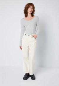 Camisa de mangas compridas cinza claro combinada com calças largas de cintura alta em branco sujo. Sapatos pretos com sola grossa e detalhe em meias vermelhas.