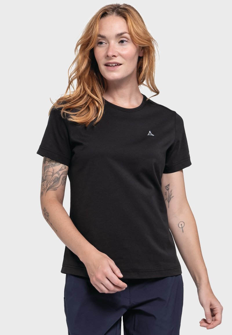 Schwarzes Baumwoll-T-Shirt mit Rundhalsausschnitt, kurzen Ärmeln und einem kleinen Logo-Detail auf der Brust, getragen mit navyblauen Hosen. Glatte Textur.