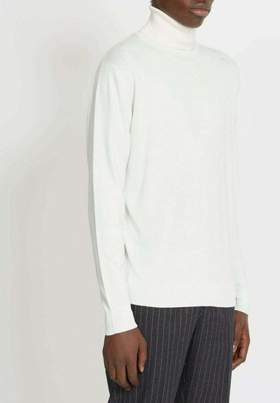 Maglione a collo alto color crema chiaro in morbido punto coste. Presenta maniche lunghe e una silhouette aderente, abbinato a pantaloni scuri a righe sottili.