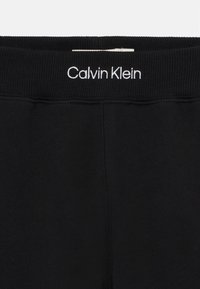 Cinturilla negra con el logo blanco de "Calvin Klein". Tejido suave, textura lisa, diseño elástico. Costuras visibles a lo largo de las costuras.