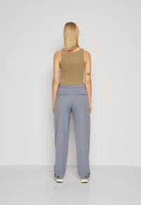 Tan tanktop en lichtgrijze wijde broek, met achterzakken en knoopaccenten op de zoom. Glad textuur, ontspannen pasvorm.