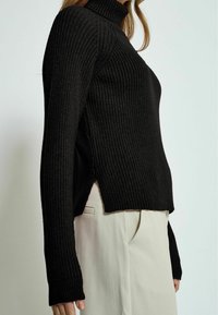 Schwarzer gerippter Rollkragenpullover mit langen Ärmeln, seitlichen Schlitzen und taillierter Passform, aus einem strukturierten Strickstoff gefertigt.