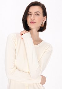Cremfarbener Cardigan aus weich gestricktem Stoff, mit rundem Halsausschnitt, langen Ärmeln und Knöpfen entlang der Vorderseite.