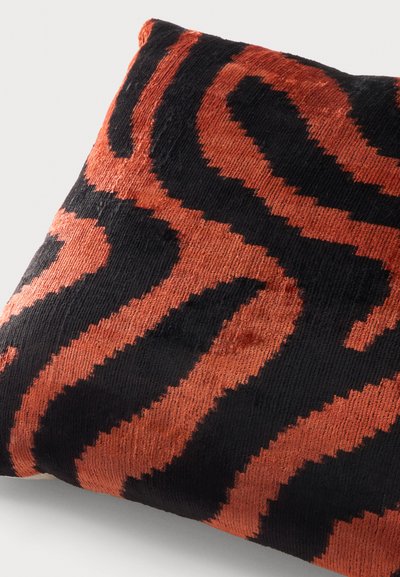 Coussin carré avec un tissu doux et texturé présentant un motif abstrait en zigzag noir et orange.