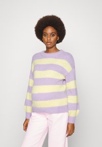 Suéter tricotado em listras lavanda e amarelas. Apresenta um decote redondo e mangas balão. Combinado com calças rosa-claro. Textura suave.